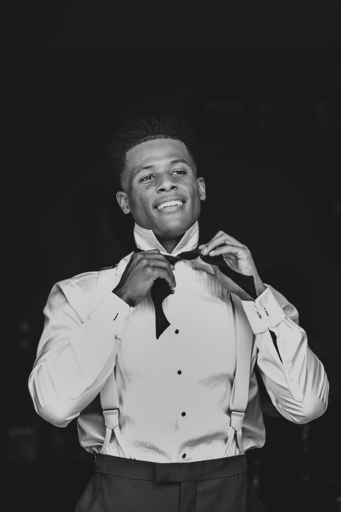 Groom in tux does up bow tie during prep at The Barns at Lodge Farm Essex documentary wedding photographer