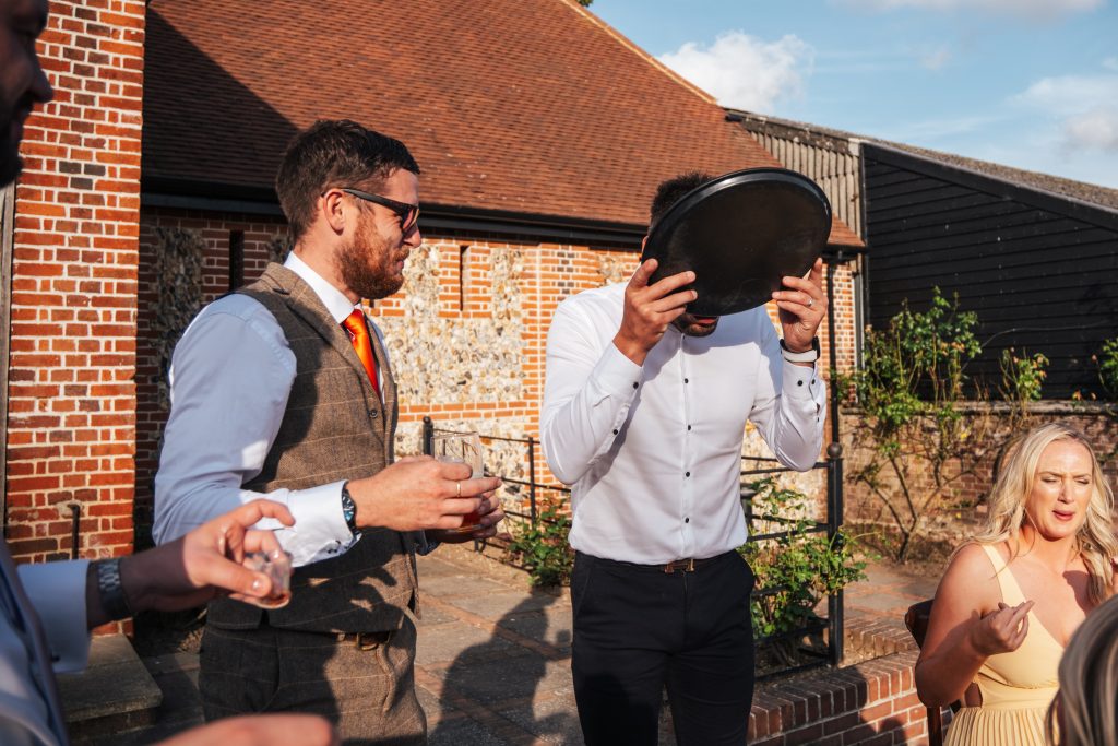 Guest drinks spilled drink from tray as others laugh at Tuffon Hall Essex documentary wedding photographer