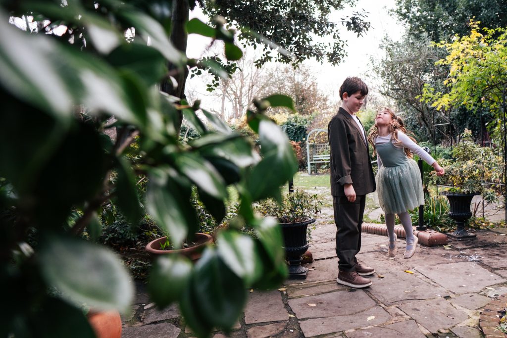 Little girl jumps up into boys face in garden after London wedding ceremony Essex documentary wedding photographer