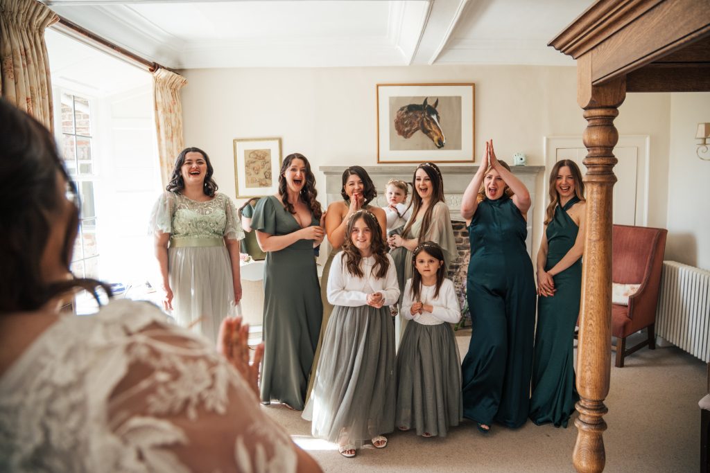Laughing, clapping bridesmaids in green react to bride in her dress at Bruisyard Essex documentary wedding photographer